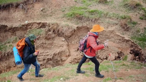Two hikers moving carefully along edge of ravine, avoiding steep drop and Stock Footage 333471493