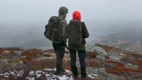 Two hikers stand on a rugged mountain ridge staring into the misty wilderness Video stock 318197345