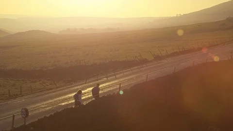 Two hikers walk toward sunset on lonely road in beautiful landscape Stock Footage 105303486