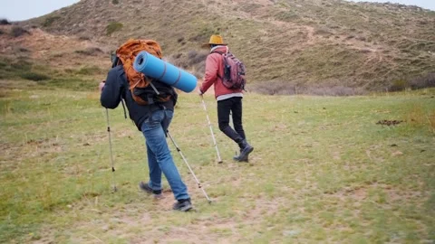 Two hikers walking across open valley with backpacks and trekking poles Stock Footage 333471560