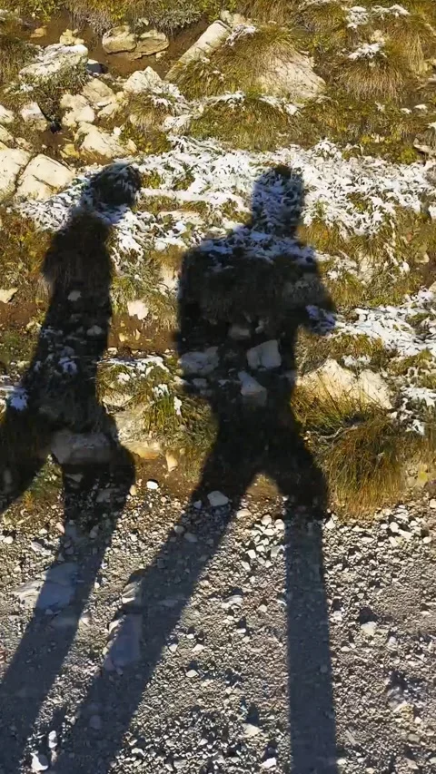 Two hikers walking along trail casting long shadows in Dolomites mountains. Stock Footage 330437397