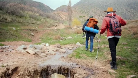 Two hikers walking forward after crossing rough terrain and ravine, showing Stock Footage 333471444