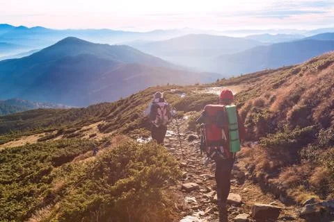 Two Hikers walking on Mountain Path Sunset Mountains Background Stock Photos