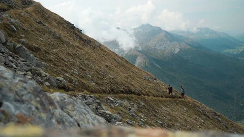 Two hikers walking up steep mountain towards camera in alpine mountain landscape Stock Footage 129615742
