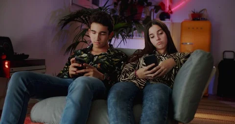 Two Hispanic friends feeling bored using black smartphone during late evening at Stock Footage 120947570