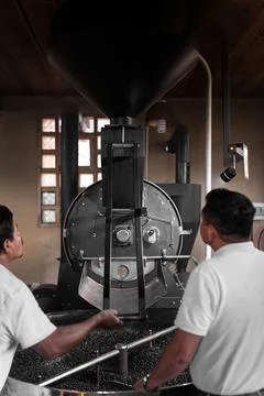 Two Hispanic men are operating the lever of a coffee roaster machine Stock-Fotos