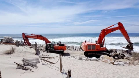 Two Hitachi excavators work on a coastal erosion protection project on a beach i Stock Footage 335181681