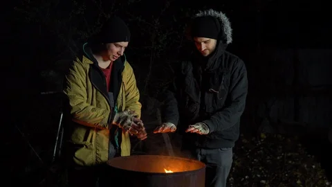 Two homeless young men bask in the fire. Men stand near a barrel of fire at Stock Footage 129557792