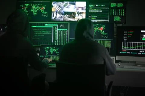 Two hooded hackers hacking security firewall late at night in basement hideout Stock Photos