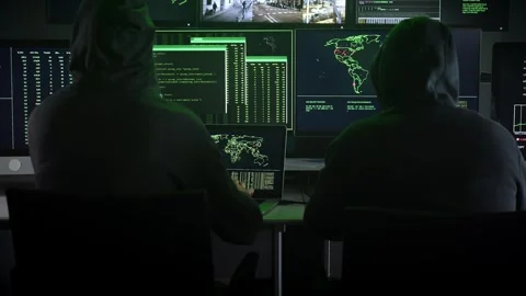 Two hooded hackers work together computer viewing maps data on display screens 库存影片 244595918