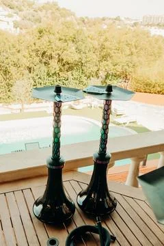 Two Hookahs placed on a wooden table with a view of a swimming pool and green Stock Photos
