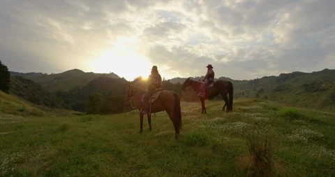 Two horseback riders pause on a hillside at sunset, New Zealand Видео 102925867