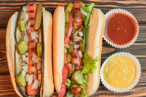 Two hotdog, one with ketchup, one with mustard on wooden background Stock Photos