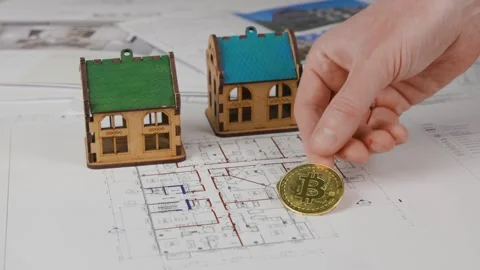 Two house models are on blueprints, and a man's hand is placing bitcoins Stock Footage 305638746