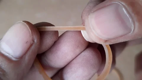 Two human hands pulling and stretching a single brown elastic rubber band s.. Stock Footage 324825051