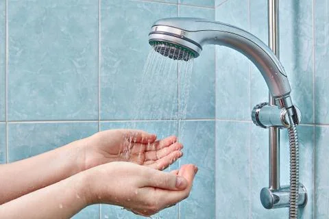 Two human palms under rain shower head with handheld sprayer. Stock Photos