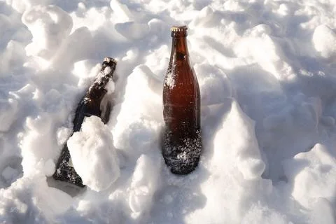 Two ice cold brown beer bottles in fresh white snow in the sun background Stock Photos