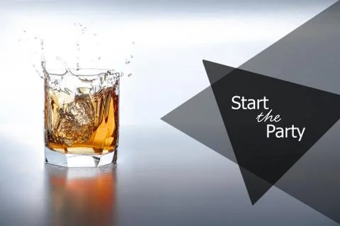 Two ice cubes fall into a glass of whiskey. With logo: start the party. Stock Photos