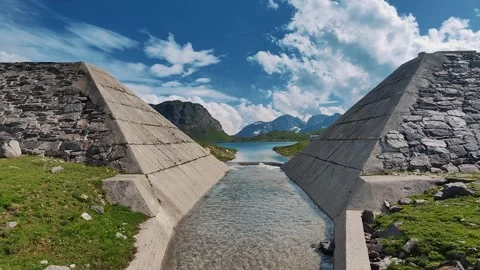 Two imposing concrete structures framing a clear, narrow stream that leads to a Stock Footage 306157661