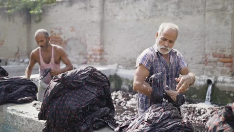 Two Indian labourers removing a long sheet of colored print cloth out of water Stock Footage 149301691