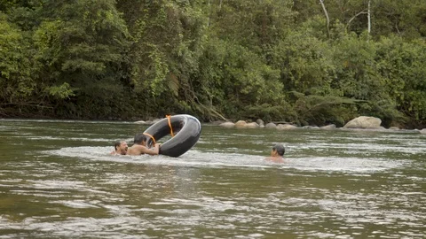 Two indigenous boys and a foreign adult are holding on to a floating tire before Stock Footage 113179545