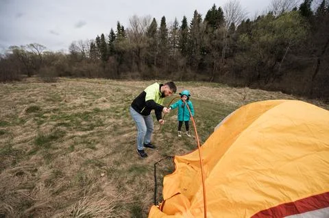 Two individuals are engaged in the process of erecting a vibrant, orange tent Stock Photos