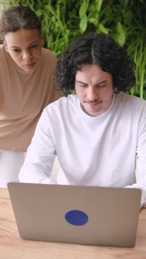 Two individuals are focused on a laptop screen in a space filled with plants. Th Stock Footage 346150790