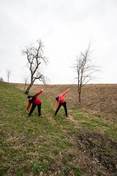 Two individuals dressed in vibrant red stretch their arms in unison on a gras Fotos de archivo