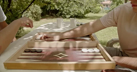 Two individuals enjoying a game of backgammon on a sunny day, seated outdoors Stock Footage 282560979