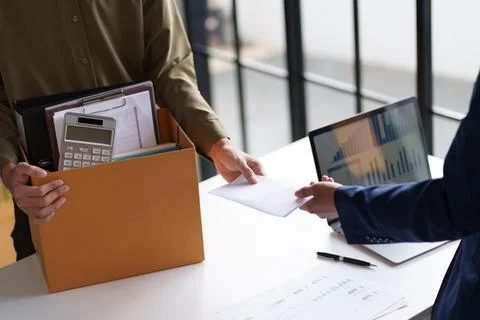 Two individuals exchanging documents across a desk. One person is holding a.. Stock Photos