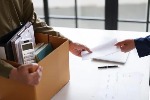 Two individuals exchanging documents across a desk. One person is holding a.. Stock Photos