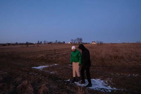 Two individuals explore a rural field at dusk, surrounded by empty terrain and Stock Photos