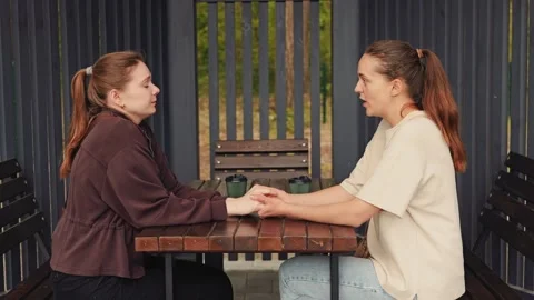 Two individuals sit across from each other at a table in an outdoor area. They 動画素材 336447428