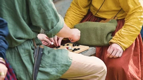 Two individuals sit on the ground, focused on a board game in an outdoor setting Stock Footage 345033808