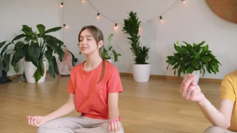 Two individuals sit in meditation in a bright room filled with plants. Soft ligh Stock Footage 346149553