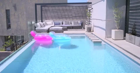 Two inflatable floats drifting across rooftop pool under gentle breeze, showing Stock Footage 341665524