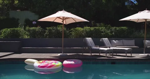 Two inflatable rings are drifting leftward near pool edge as light breeze is Stock Footage 340454627