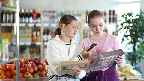 Two interested shoppers scan the barcode on phone and read the information and Stock Footage 335618426