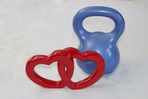 Two interlocking red hearts beside blue kettlebell on white background Stock Photos
