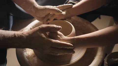 Two intertwined hands form a pot of clay on a potter's wheel. A male hand helps Stock Footage 102247665