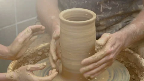 Two intertwined hands form a pot of clay on a potter's wheel.  Stock Footage 106111461