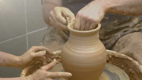 Two intertwined hands form a pot of clay on a potter's wheel. A male hand helps  Stock Footage 106631948