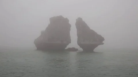 Two isolated limestone karsts tower above calm and misty Halong Bay. Stock-Footage 74327939