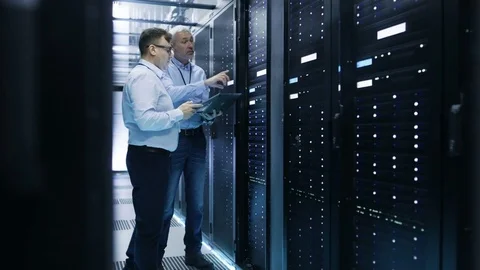 Two IT Engineers Standing in Working Data Center. They Use Laptop and Tablet  Stock Footage