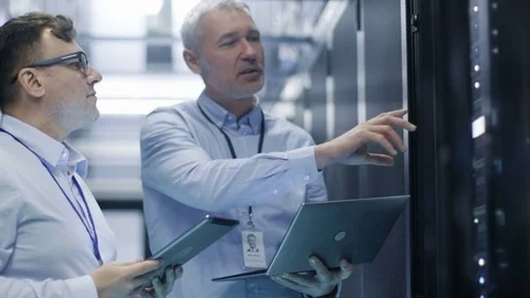Two IT Technicians Standing in Working Data Center. They Use Laptop and Tablet  Stock Footage