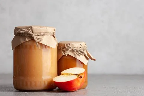 Two jars of apple jam with half an apple on gray surface. Space for text Stock Photos