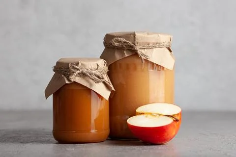 Two jars of apple jam with half an apple on gray background Stock Photos