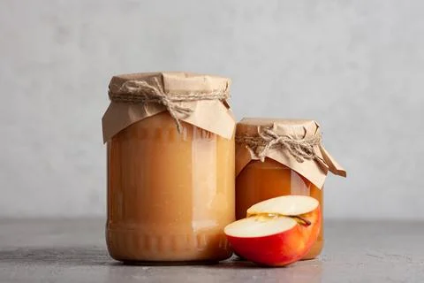 Two jars of apple jam with half an apple on gray surface Stock Photos