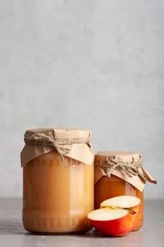 Two jars of apple jam with half an apple on gray surface Stock Photos