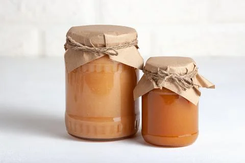 Two jars of apple jam in rustic wrapping on a light background Stock Photos